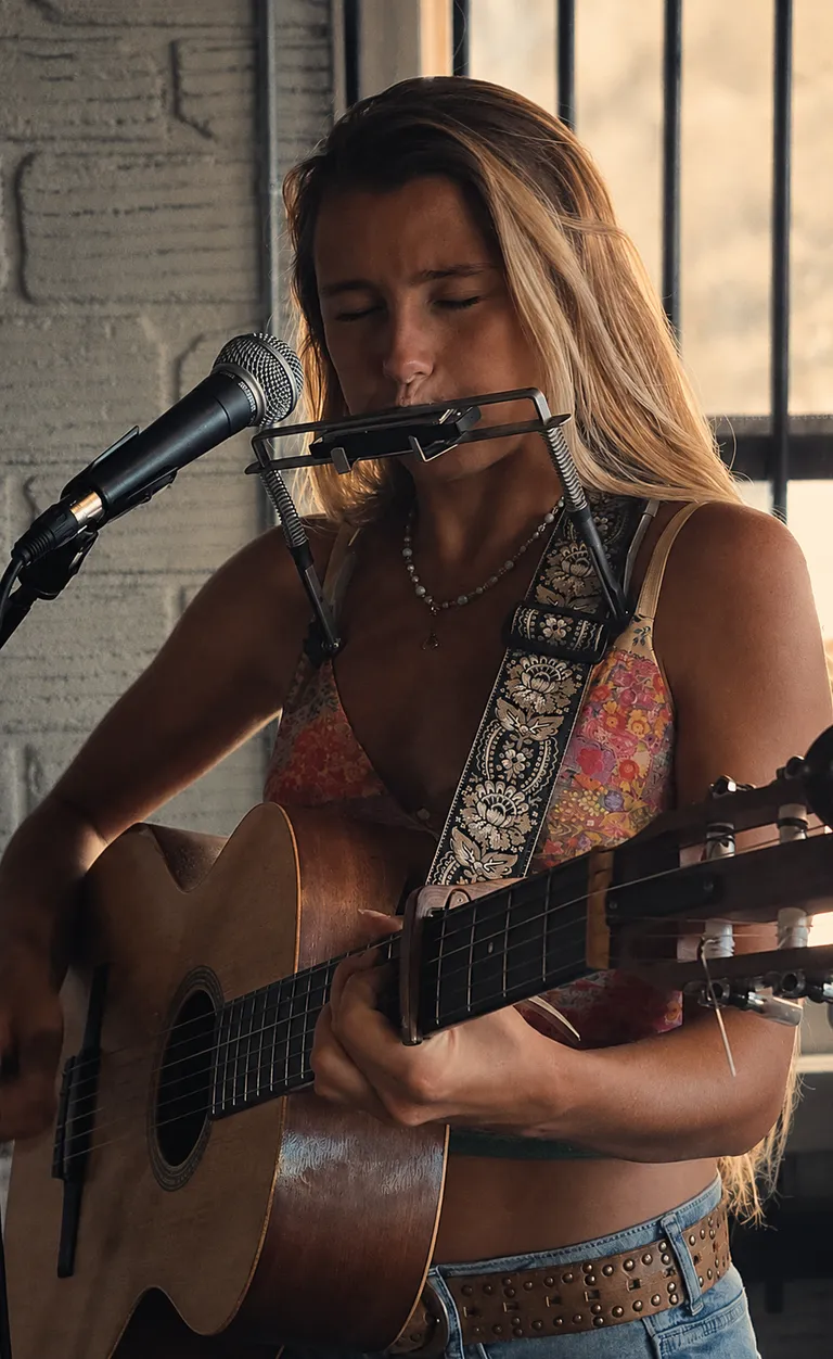 Lucy Spotts playing harmonica and acoustic guitar.